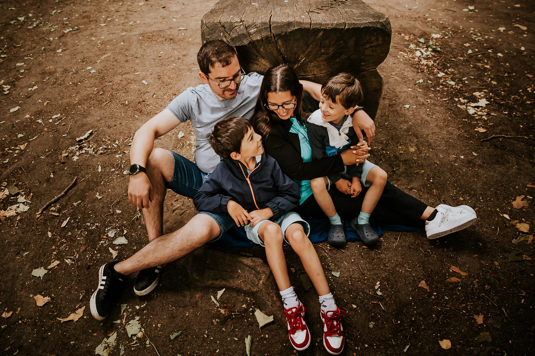 Une famille assise, riant ensemble lors d’une séance photo dans une forêt du Val-de-Marne.