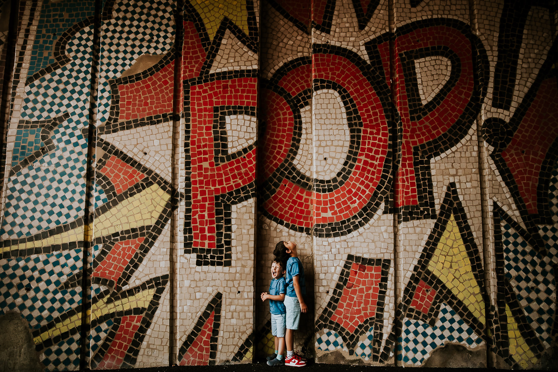 Deux enfants debout devant une fresque pop art colorée avec le mot "POP", échangeant un regard complice dans un décor vibrant.